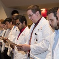 Crowd in white coats stands and reads from cards