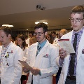 Crowd in white coats stands and reads from cards