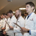 Crowd in white coats stands and reads from cards