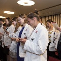 Crowd in white coats stands and reads from cards
